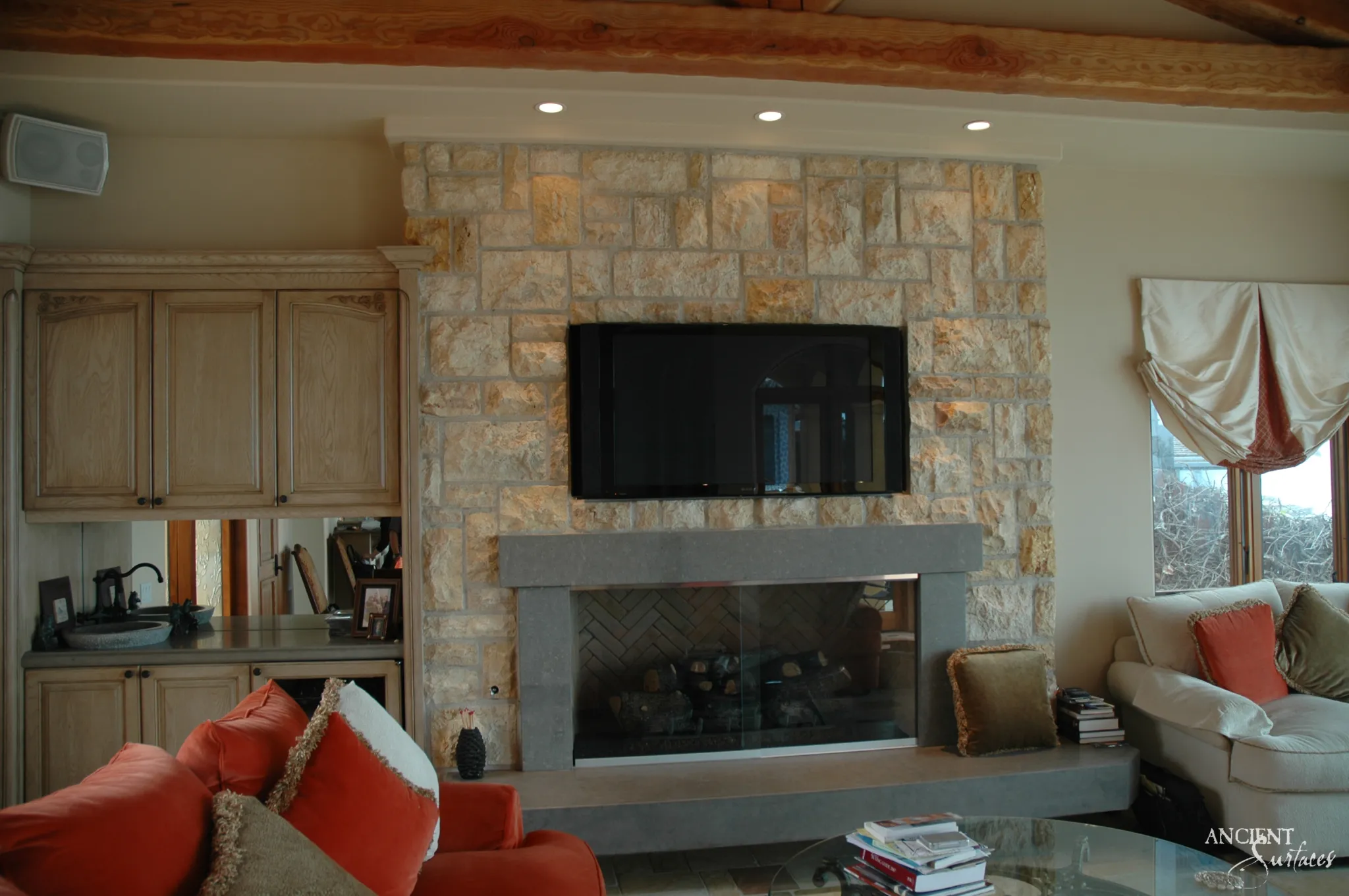 Reclaimed limestone fireplace wall from Ancient Surfaces with a linear stone mantel and hearth in a beamed family room