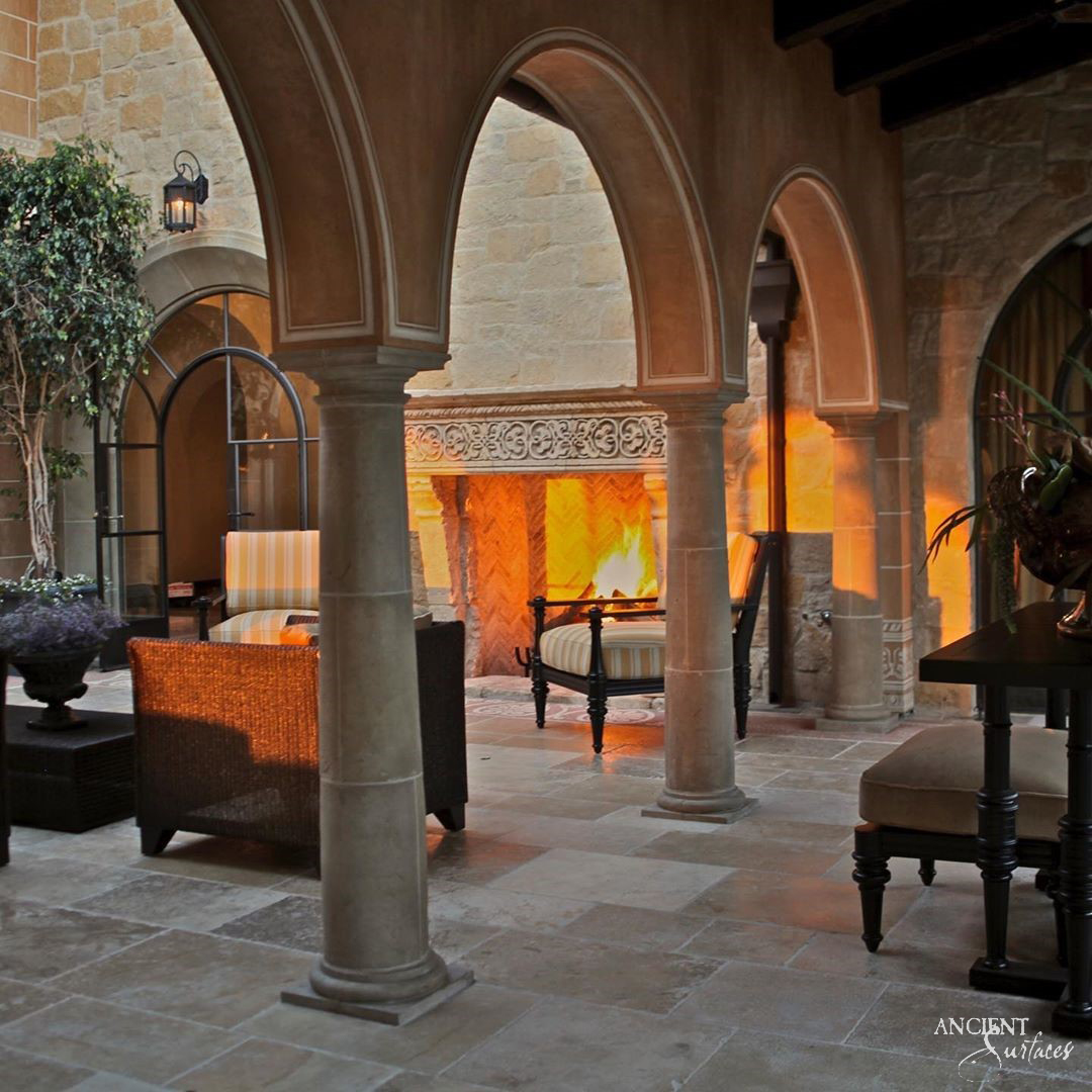 Reclaimed antique limestone fireplace mantel from Ancient Surfaces with a carved foliate frieze burning in an arcaded outdoor loggia