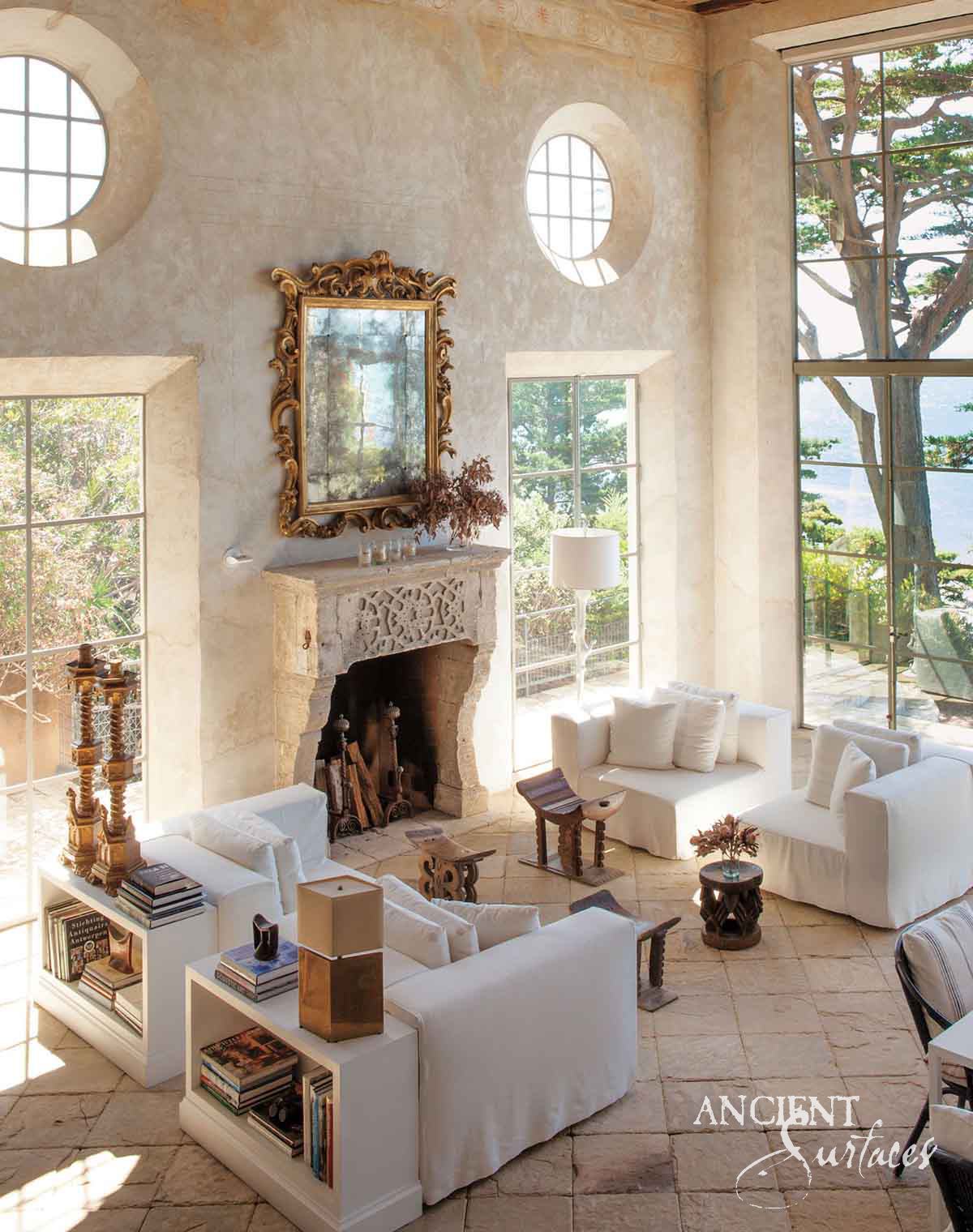 Ornate reclaimed antique limestone fireplace mantel from Ancient Surfaces with a pierced foliate frieze beneath a gilt mirror in a double height coastal room